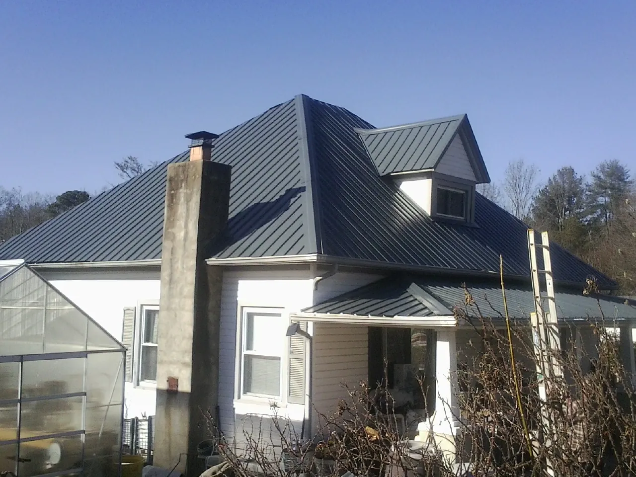 Dark blue standing seam metal roof on a white farmhouse with dormer — Slate & Tile Roof Repair by Roofing Brothers in Burgess