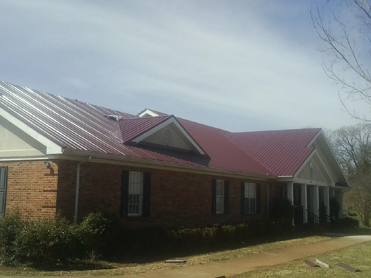 Red metal roof with gabled entries on a long brick building, from a Hail Damage Roof Repair job in Burgess