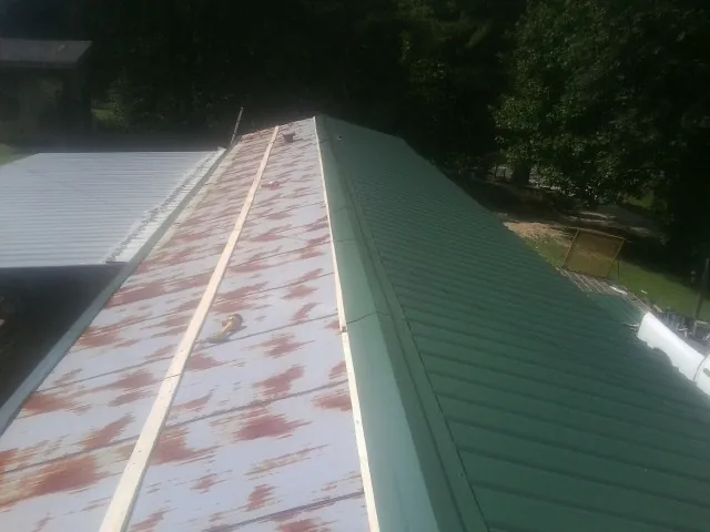 Old rusted panels beside newly installed green metal roofing — Wind Damage Roof Repair by Roofing Brothers in Burgess