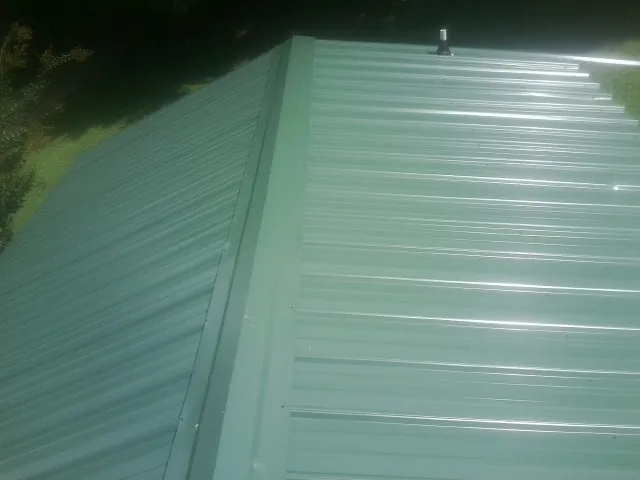 New green metal panels meeting at the ridge of a roof — Flat Roof Repair work by our crew in Burgess