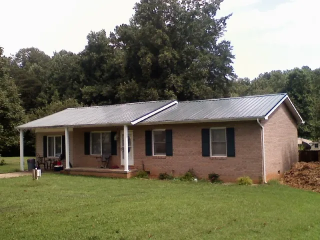 Gray metal roof on a brick ranch house with a side carport in Burgess