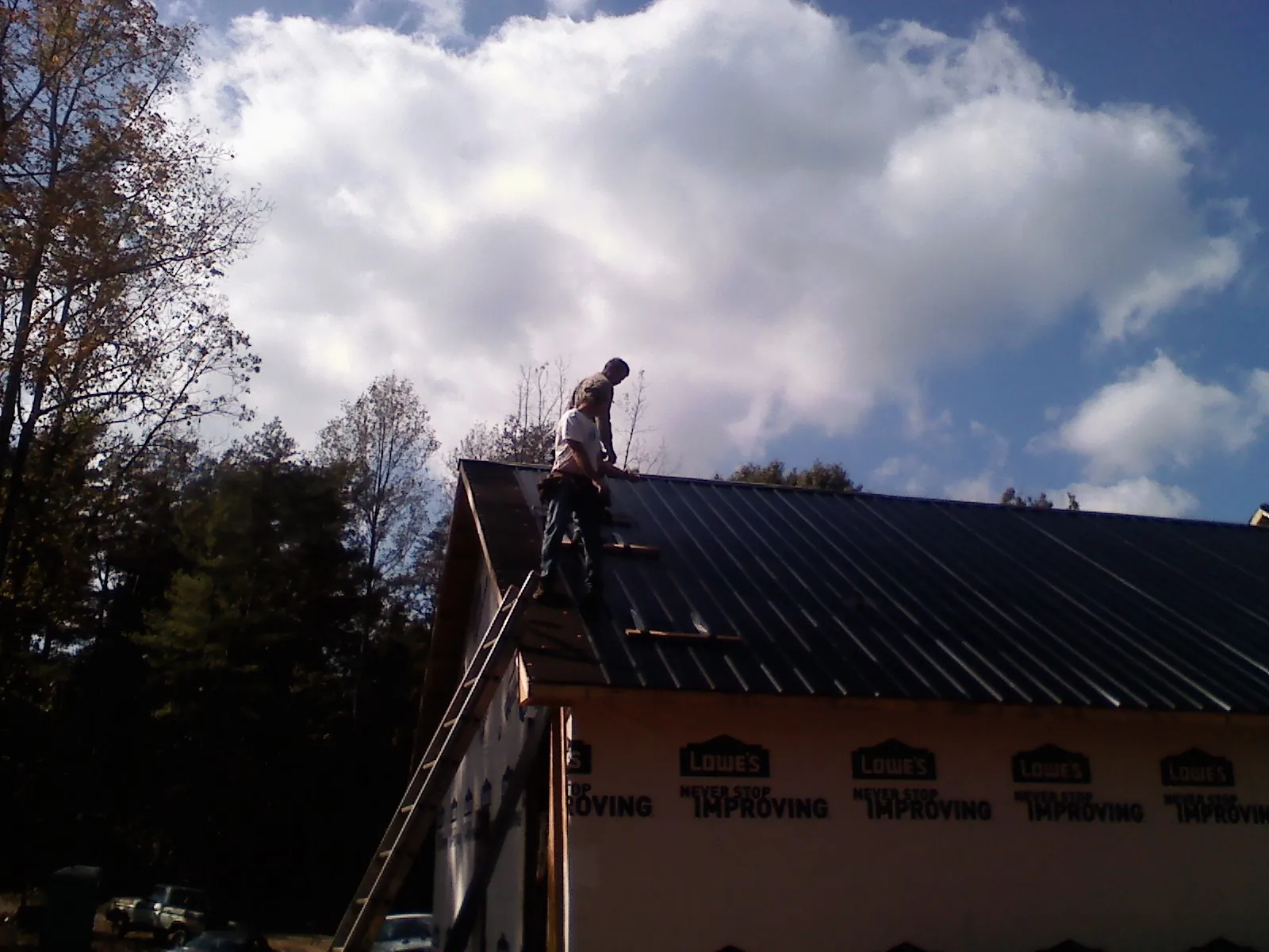 Roofer fastening dark metal panels high against a cloudy sky, from a Roof Inspection job in Burgess