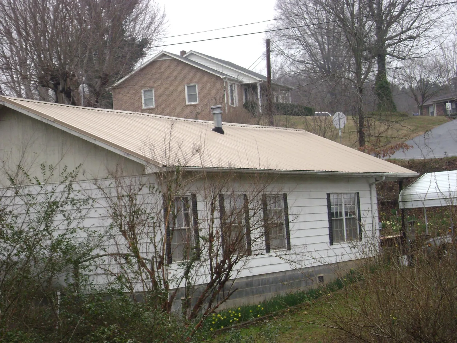 Tan metal roof on a white sided house set into a hillside — Commercial Roofing by Roofing Brothers in Burgess