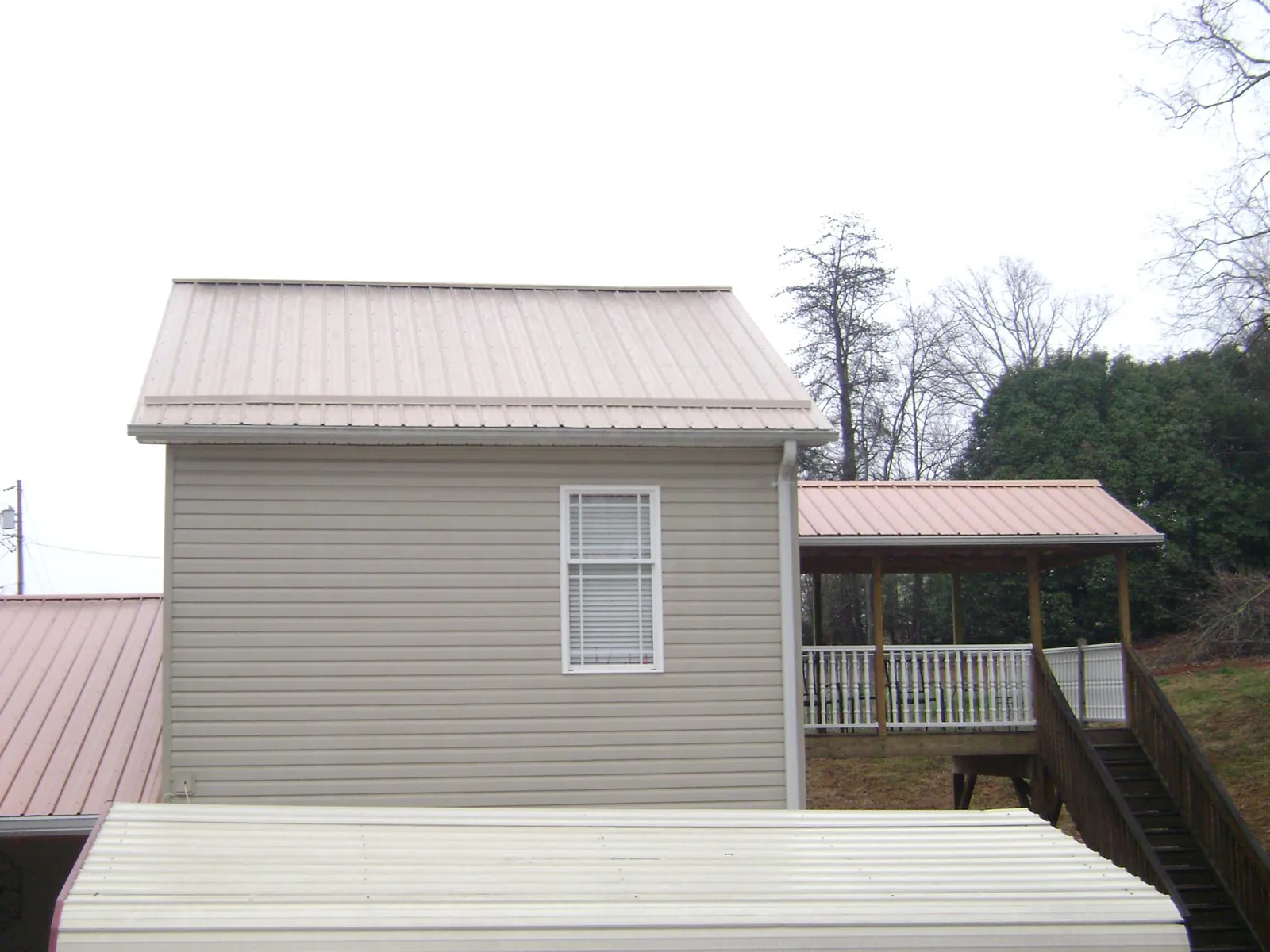 Tan metal roofs on a two story addition and attached porch, from a Roof Replacement job in Burgess